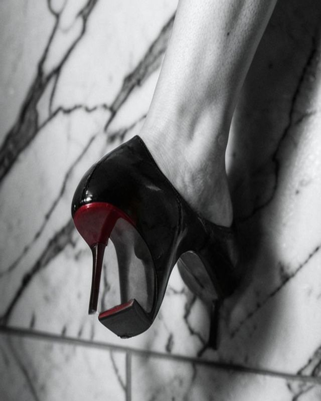 Redonnoir Fine-Art Foto ‚Kalter Marmor, heißes Rot‘ — elegante Frau in Schwarz mit rot lackierter Stiletto-Sohle, Cold Marble, Hot Red, editorial Schwarzweiss mit rotem Farbakzent.